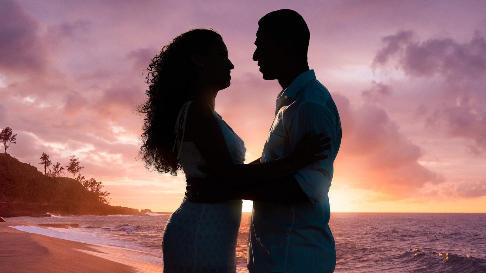 Couple embracing in silhouette on a beach at sunset, facing each other by the sea